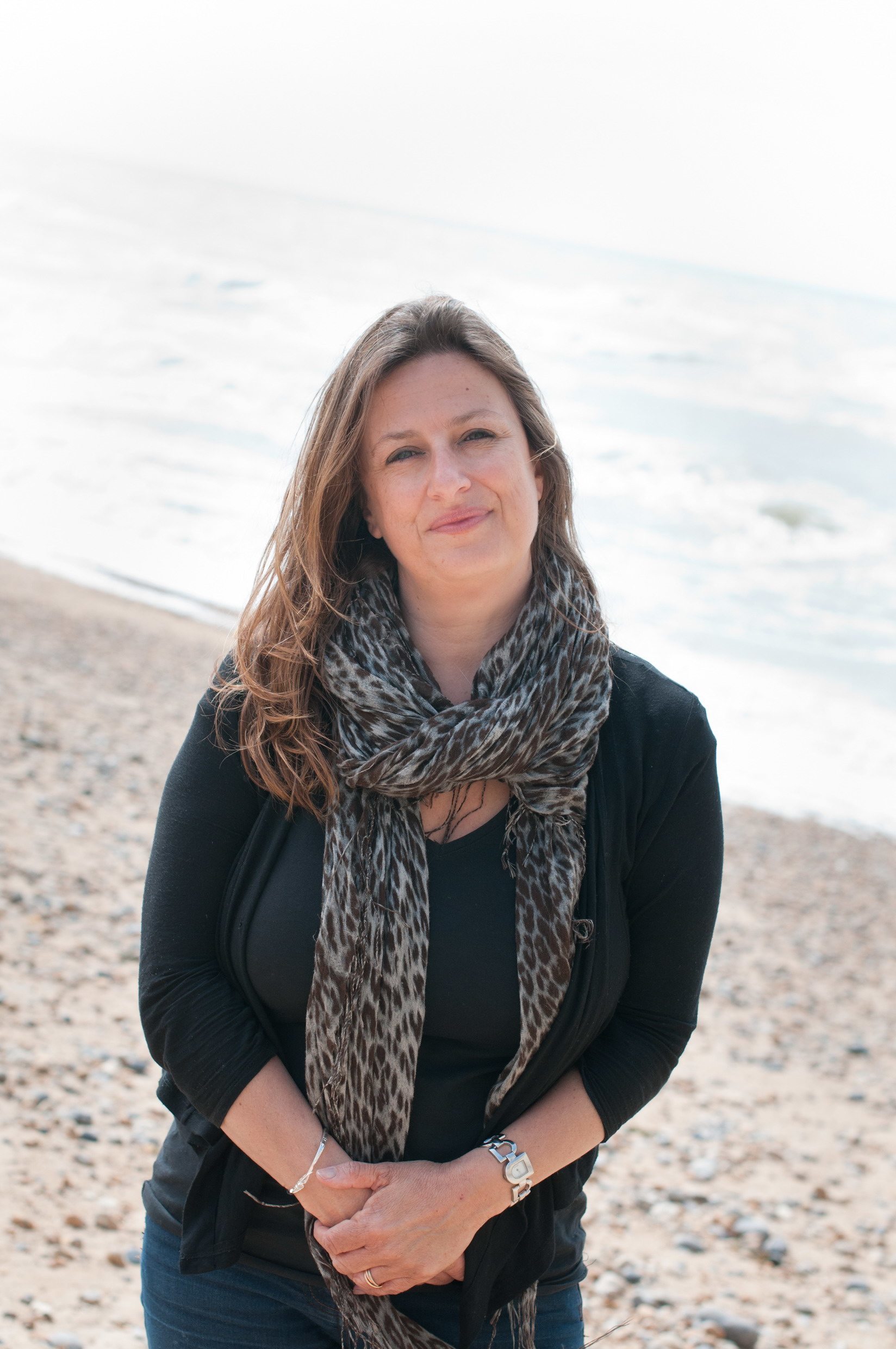 An image of the author Elly Griffiths on a beach wearing a scarf.